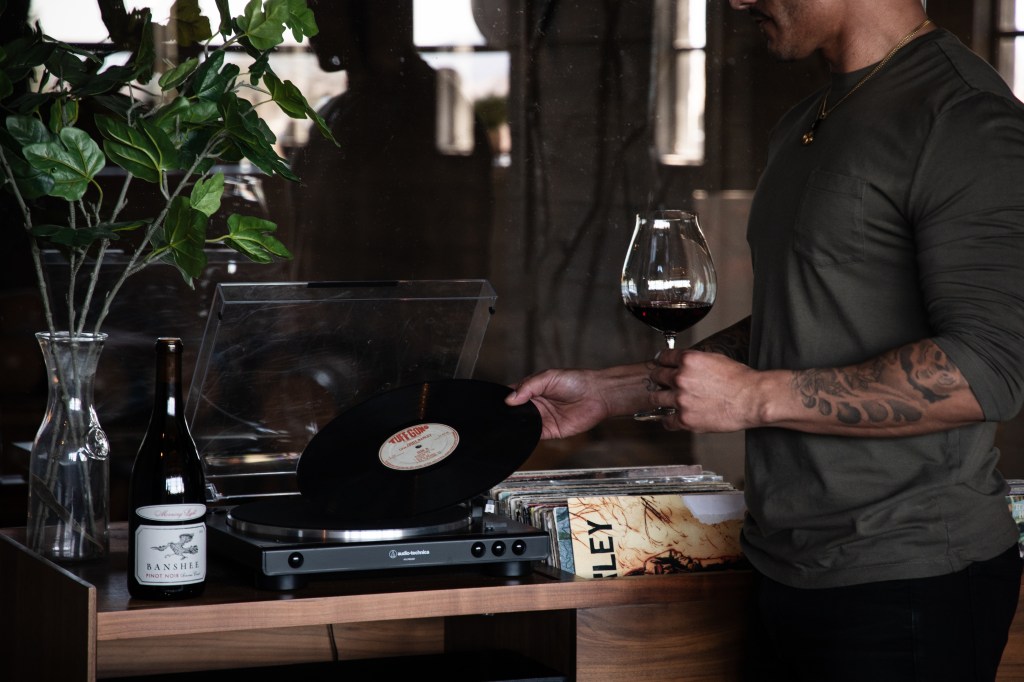 Final Friday at Banshee - Man Putting Record on Player with Glass of Wine